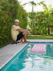 A skater sits on the edge of a pool, gazing peacefully at vibrant pink floaties.