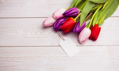 Multicolor tulip bouquet is lying on painted wooden plank in flat design with blank gift tag
