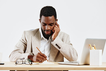 Professional man working at desk with laptop and notebook, wearing beige blazer and white shirt,...