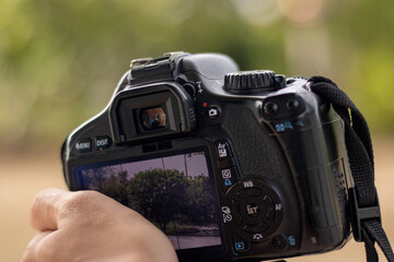 A photographer's hand holds a DSLR camera, framing a landscape shot on the LCD screen. A...