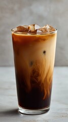 Tall glass of iced coffee with ice cubes, showcasing beautiful layers of dark coffee and light cream, set against a neutral background. Ideal for caf&eacute; promotions, beverage - related content, and coffe