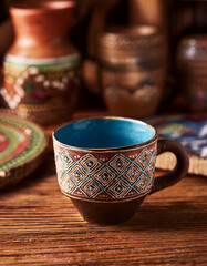 A hand-crafted ceramic coffee cup with traditional patterns, placed on a carved wooden table with local art pieces in the background