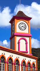 Colorful facade of a building with a tower and a clock against a blue sky with clouds....