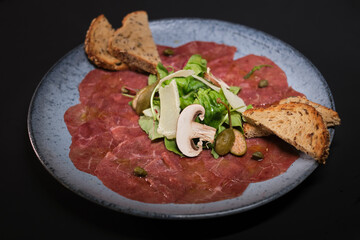 Slices of prosciutto on a blue plate on a dark background. Top view with copy space