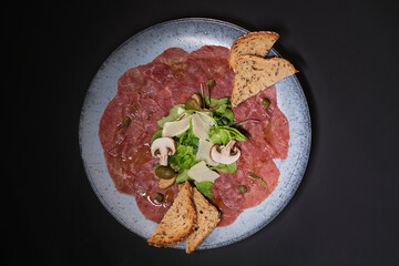 Slices of prosciutto on a blue plate on a dark background. Top view with copy space
