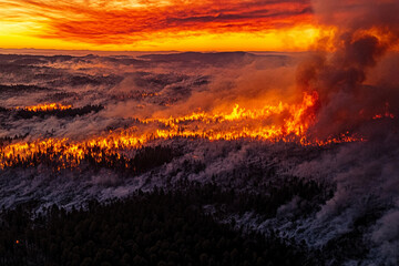 Aerial view of forest fire in mountainous area at sunset with beautiful winter landscape contrast