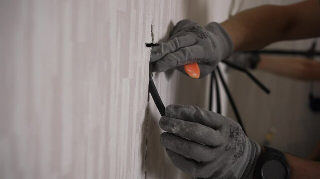 Professional electrician carefully inserts electrical cables into a prepared slot in the wall, using a plastic tool to ensure proper placement and secure the cables for subsequent plastering