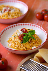 Top view of plates with pasta on red wooden table, surrounded by cheese and tomatoes. Traditional Italian food, rustic homemade meal.
