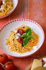 Top view of plates with pasta on red wooden table, surrounded by cheese and tomatoes. Traditional Italian food, rustic homemade meal.