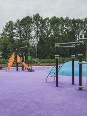 Vertical photo of colorful modern playground with climbing structures and slide on purple rubber...
