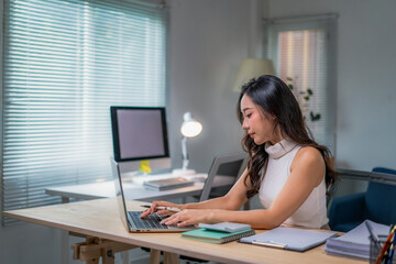 woman is sitting at a desk with a laptop and a computer monitor