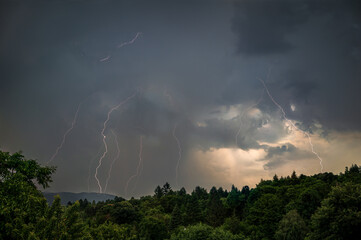 Dramatic Thunderstorm with Lightning Strikes Illuminating Dark Sky over Forest Landscape