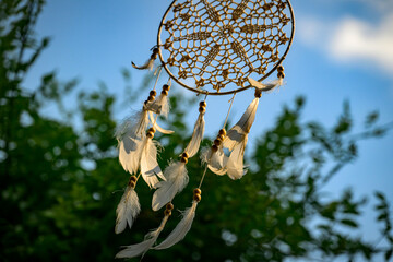 Dreamcatcher with White Feathers Swaying Outdoors Against Blue Sky and Green Trees