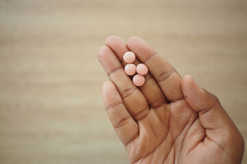Hand holding four pink pills on a wooden surface