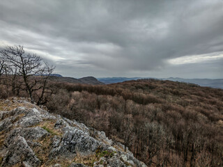 Limestone rocks and leafless trees frame a panoramic view of the undulating hills and cloudy sky at...