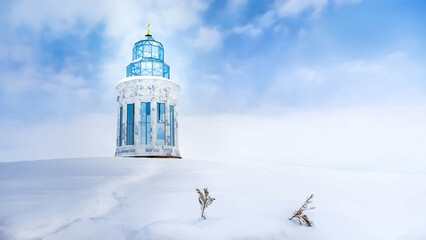 A beautiful winter landscape with the modern glass chapel of the Armenian Alphabet Monument in Artashavan, Armenia, standing on a hill completely covered in deep snow under a cloudy blue sky