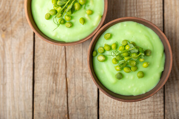 Green pea soup on a wooden table. Fresh pea soup bowl. Delicious healthy cream soup in a bowl with green peas and croutons. Healthy vegan puree. Copy space. Space for text.