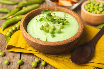 Green pea soup on a wooden table. Fresh pea soup bowl. Delicious healthy cream soup in a bowl with green peas and croutons. Healthy vegan puree. Copy space. Space for text.