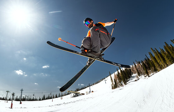 Bottom view of a skier jumping with crossed skis against a blue sky and bright sun, ski resort, low angle view
