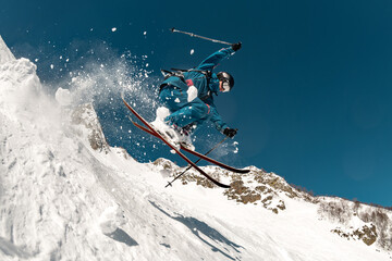 A skier performs a risky trick with a high jump, sliding down the mountain off-piste, with cloud of...
