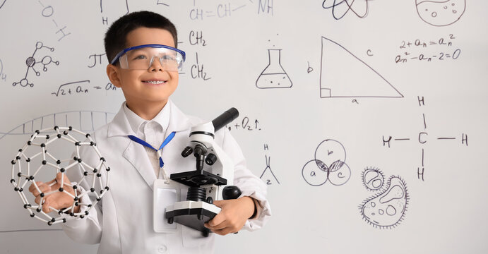 Cute little boy with molecular model and microscope in chemistry classroom