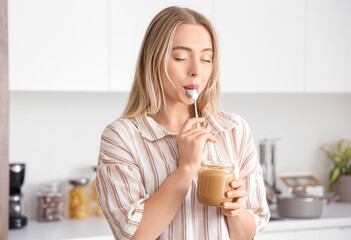 Young woman eating tasty nut butter in kitchen