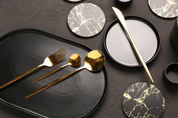 Clean plates, drink coasters and golden cutlery on black grunge table