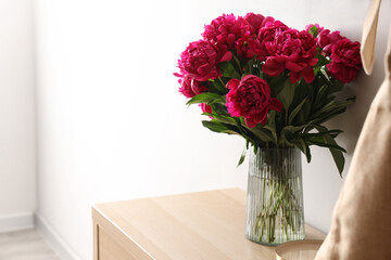 Vase of red peonies on dresser near light wall