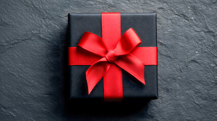 Black gift box with a red ribbon on a dark background, top view. Copy space.