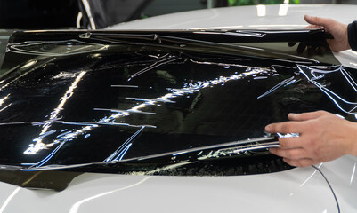 Applying tinting foil on a car window in the tuning studio. Male car service worker glue window...