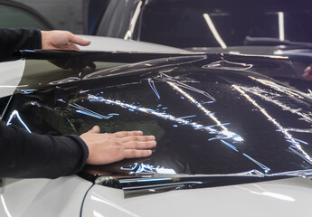 Applying tinting foil on a car window in the tuning studio. Male car service worker glue window...