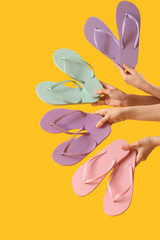 Hands with many different flip-flops on yellow background