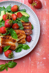 Plate of summer salad with fresh strawberries, arugula, and grilled halloumi cheese. Bright, flavorful, and healthy dish perfect for warm seasons.