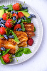 Plate of summer salad with fresh strawberries, arugula, and grilled halloumi cheese. Bright, flavorful, and healthy dish perfect for warm seasons.