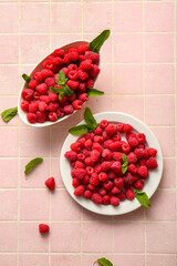 Plate and bowl with fresh raspberries on pink tile background