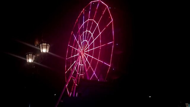 Ferris Wheel with Neon Red and Pink Lights at Night &ndash; Side View with Street Lamps