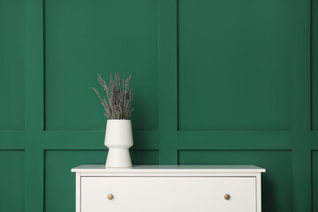 Vase with lavender on white chest of drawers near green wall