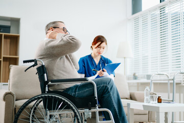 A caring nurse in blue scrubs conducts a neck pain consultation with a senior wheelchair patient at...
