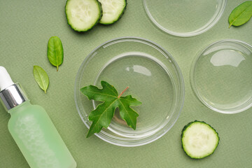 Petri dishes with cucumber pieces, herbs and bottle of cosmetic product on green background