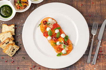 Plated tomato and mozzarella arrangement garnished with basil and herbs