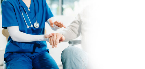 A compassionate nurse in blue scrubs holds the hand of a senior patient in a hospital clinic,...