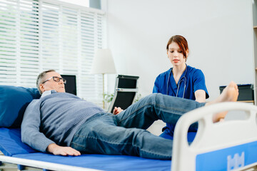 A nurse in blue scrubs guides a senior patient through leg mobility exercises on a therapy bed,...
