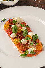 Plated tomato and mozzarella arrangement garnished with basil and herbs