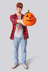 Scary zombie man with Halloween pumpkin on grey background