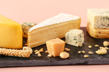 Board with tasty cheese, nuts and grissini on pink background