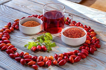 Ripe rose hips and prepared drink in glass mug, with two bowls of dried crushed rose hips. Healthy beverage for child. Two fractions of crushed berries, coarse and fine