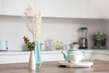 Wooden table with tea set, dried flowers and eucalyptus branches in modern kitchen, closeup