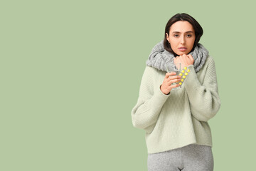 Sick young woman with pills and glass of water on green background