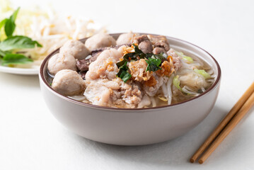 Thai noodles soup with sliced pork, minced pork, meatball and liver in a bowl eating with fresh vegetables on white background, Traditional Thai street food