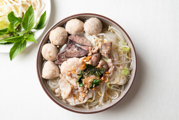 Thai noodles soup with sliced pork, minced pork, meatball and liver in a bowl eating with fresh vegetables on white background, Traditional Thai street food, Top view
